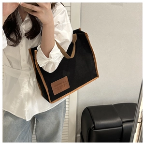 Detail of black corduroy tote bag featuring brown leather trim and fashion label