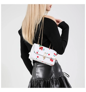 Detail of crossbody bag with cherry print, golden chain strap and metal lock clasp