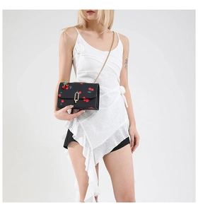 Detail of black leather crossbody bag with cherry prints and golden chain strap