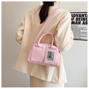 Detail of a pink PU leather shell bag showing double top handles and a clear window pocket