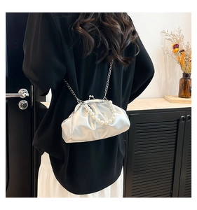 Close-up of silver pleated cloud bag with pearl handle and metal chain on model