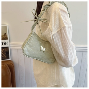 Detail of ruffled shoulder strap with bow and silver butterfly charm on green bag