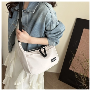 Detail of off-white nylon crescent bag with black fashion label and woven zipper pull