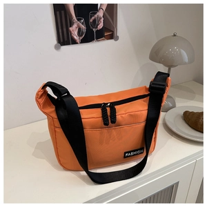 Detail view of orange nylon crossbody bag featuring black strap and fashion label