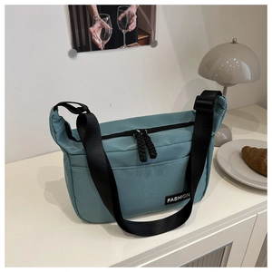 Detail of blue nylon crossbody bag with adjustable strap and Fashion label on white table