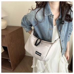 Detail view of the cream nylon dumpling bag featuring fashion label on adjustable strap