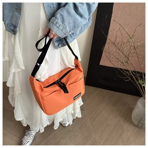 Detail of orange nylon tote bag with dual zippers and fashion label in daily setting