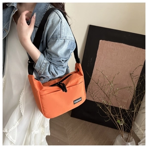Close-up of bright orange nylon crossbody bag with black strap and Fashion tag