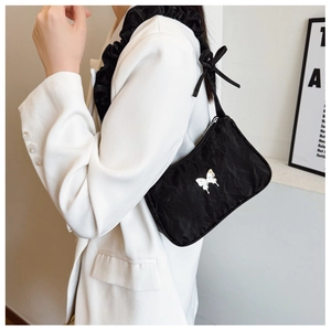 Detail of black pleated underarm bag featuring a white butterfly motif and bow strap