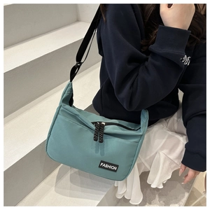 Close-up of light blue nylon messenger bag with black double zippers and FASHION patch