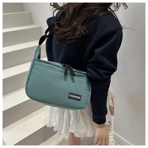 Detailed outdoor view of a cyan nylon crossbody bag with black adjustable strap and tag
