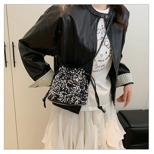 Detail shot of a sequined drawstring bucket bag styled with a leather jacket and white skirt
