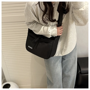 Detail of black nylon crossbody bag featuring fashion label and braided zipper pull cord