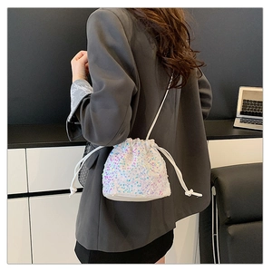 Close-up of white sequin drawstring bucket bag worn by a model in a modern office setting