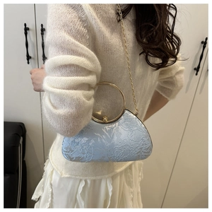 Detail of light blue floral textured handbag with golden ring handle and chain strap