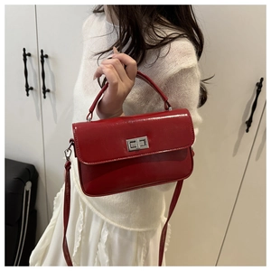 Détail du sac rouge brillant avec fermoir argenté et bandoulière sur un tricot blanc cassé