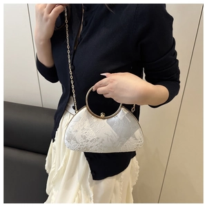 Detailed shot of white lace clutch bag with silver floral embroidery and gold ring handle
