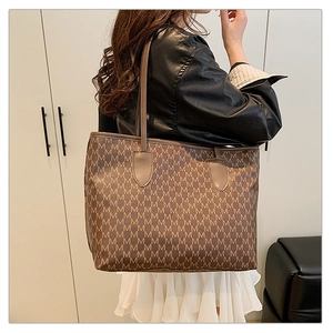Detailed view of brown tote bag with repeating M patterns and long shoulder straps