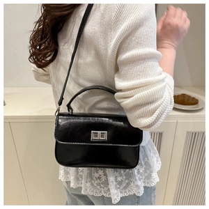Détail du petit sac à main noir brillant avec fermoir argenté porté par un mannequin