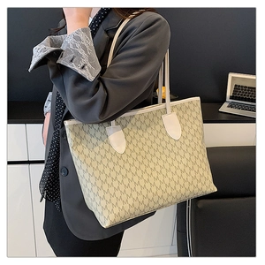 Close-up of a large beige monogram tote bag worn by a model in a modern office setting
