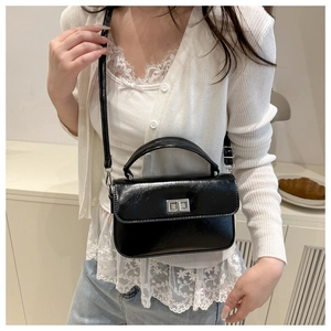 Détail d'un sac à main noir verni avec fermoir métallique argenté et bandoulière réglable