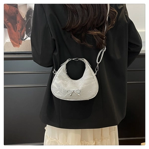 Silver metallic half-moon bag worn by a model, featuring a decorative metal bow detail