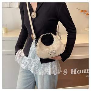 Detail of beige crescent shoulder bag with silver metallic bow and pleated texture
