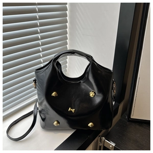 Detail of black glossy tote bag with gold bone charms and adjustable crossbody strap