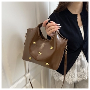 Detail of glossy brown tote bag with gold puppy motifs and detachable shoulder strap