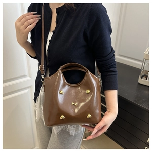Detail of glossy brown leather tote with golden decorative bone-shaped metal buckles