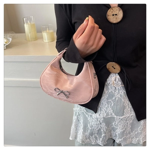 Pink pleated half-moon bag with silver metal bow detail shown in indoor setting