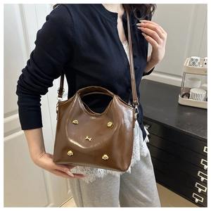 Detail of dark brown glossy leather handbag featuring golden paw and bone metal accents
