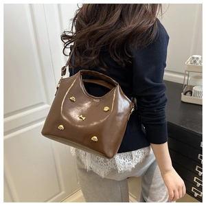 Detail of a brown leather bucket bag with gold dog and bone charms on a side-worn model