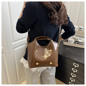 Close-up of brown leather tote bag with golden dog charms worn over the shoulder