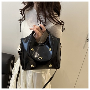 Detail of glossy black handbag with golden metal charms worn by a model in white
