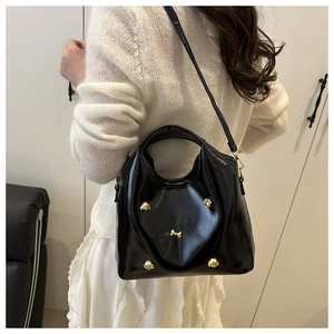 Detail of black glossy handbag featuring gold puppy rivets and adjustable strap