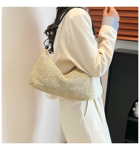 Detail of woven straw shoulder bag featuring a half-moon shape and black leather straps