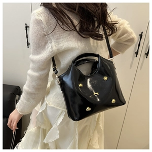 Detail of black glossy tote bag with golden dog-themed metal charms and shoulder strap