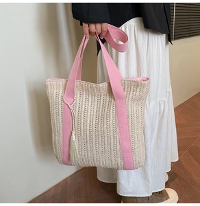 Détail d'un sac cabas en paille tissée beige avec anses roses et gland décoratif