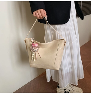 Close-up of beige leather tote bag featuring a cute plush bear charm with a plaid bow