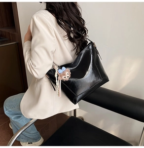 Detail of large black leather tote bag featuring a cute plush bear pendant accessory