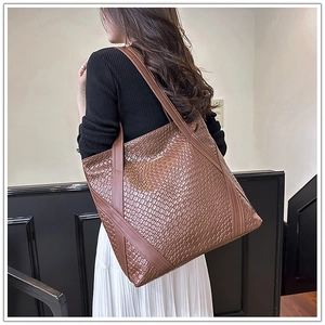 Detailed view of brown woven leather tote bag with wide shoulder strap on model