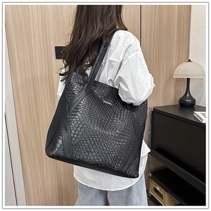 Detail of a large black woven tote bag with a gold logo on model's shoulder
