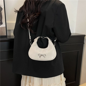 White crescent underarm bag with silver bow accent shown on model in modern setting