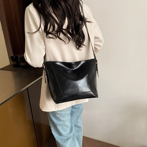 Glossy black leather tote bag shown on model in a minimalist cafe setting with gold buckle