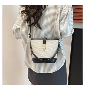 Detail view of woven bucket bag with black leather trim and golden twist lock on a model