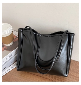 Close-up of black glossy PU leather tote bag with long straps on a wooden table