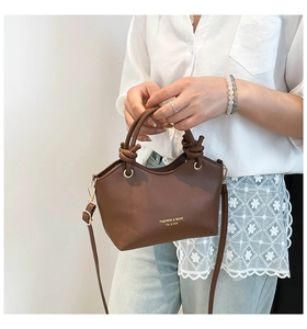 Detail of a brown lychee pattern leather bucket bag with knotted handle held by a model