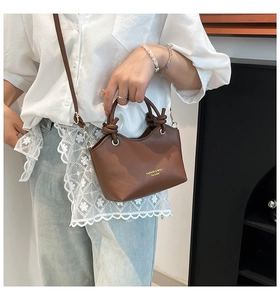 Close-up of brown litchi pattern leather bucket bag with a unique knotted top handle