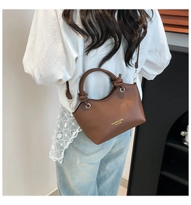 Detail of a brown lychee pattern leather bucket bag with gold hardware and knot handle